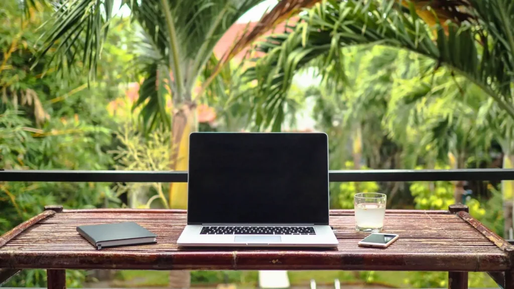 Laptop on desk with palm trees in the background.