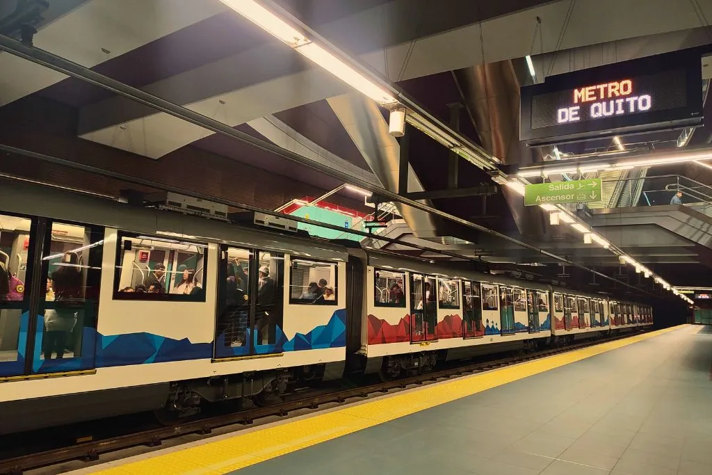 Metro cars with blue and red mountains painted on the side at the station.
