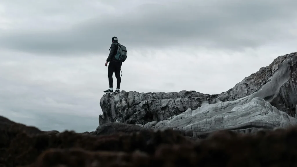 Man standing on the edge of a cliff with dark clouds rolling in.