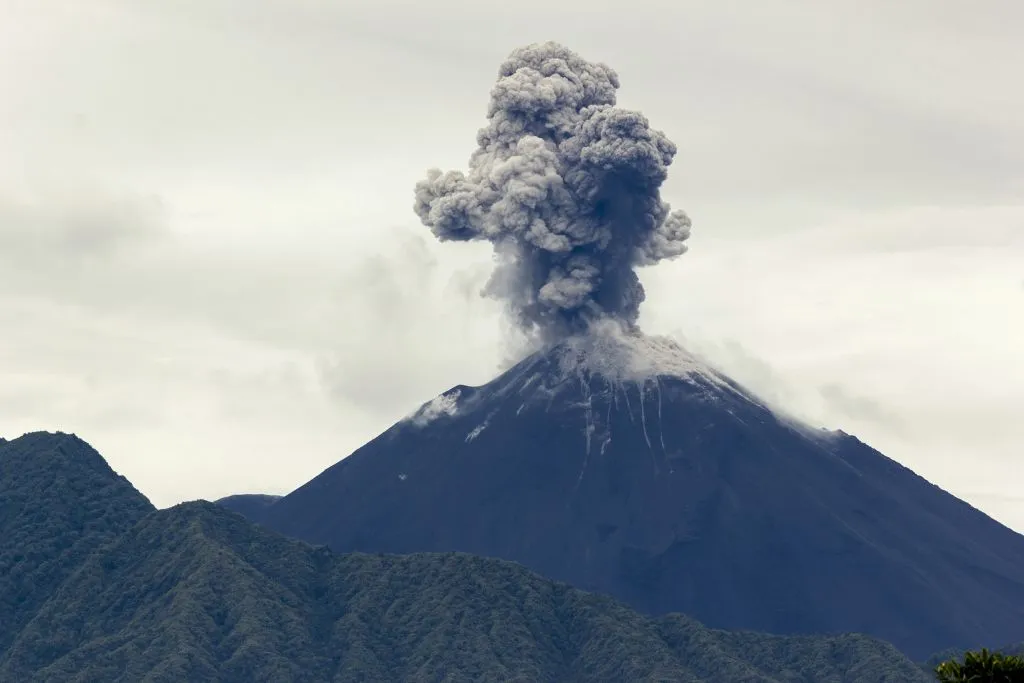 The Reventador volcano with a large plume of black and grey smoke rising from the top. It is also one of the most active volcanoes in Ecuador.